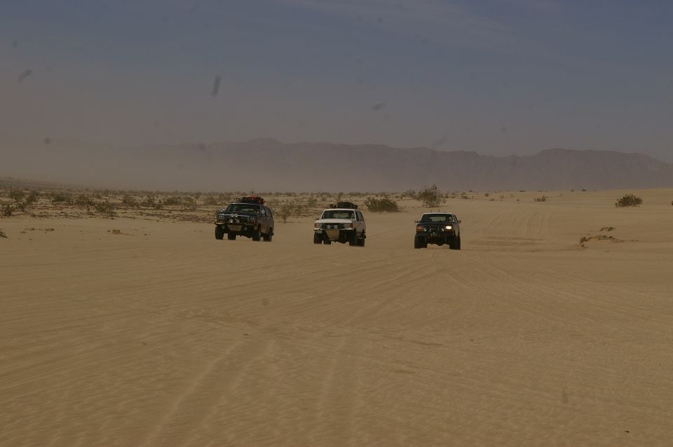 three SUVs driving across sand dunes in a desert landscape