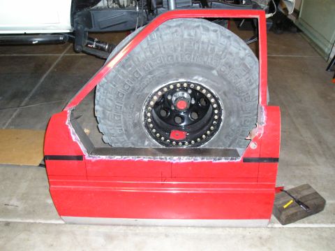 1986 Toyota Hilux - A modified red vehicle door is shown with a large spare tire fitted inside its frame.