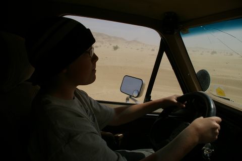1986 Ford Bronco - A child steers a vehicle through a dusty desert environment, seen from the interior.