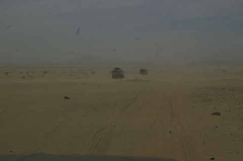 1986 Ford Bronco - Two SUVs traverse a dusty desert environment under a hazy sky.