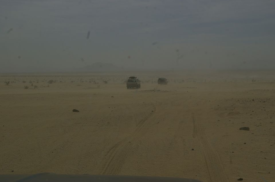 Two SUVs driving on a sandy track in a hazy desert landscape
