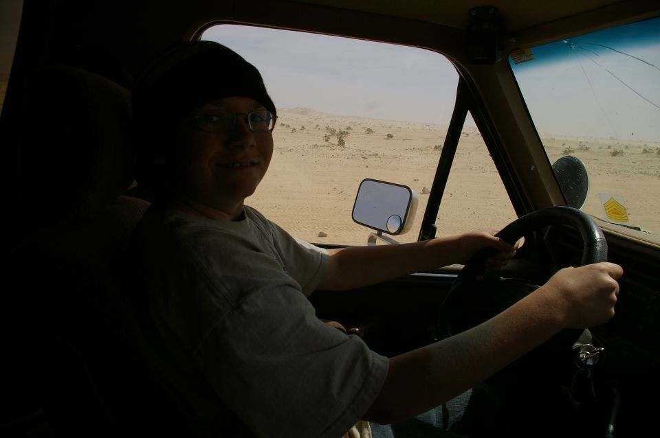 Kid wearing beanie and glasses driving a vehicle through a desert landscape