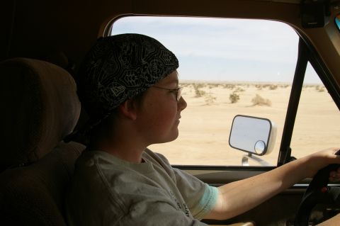 1986 Ford Bronco - A person drives a vehicle through a barren desert landscape under a bright sky.