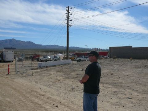 1988 Ford Bronco - A man observes a collection of vehicles and structures under a wide, cloudy sky in a dry, open area.