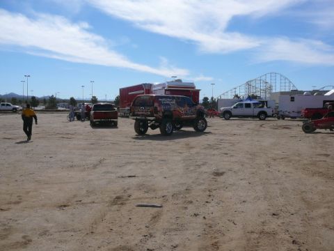 1988 Ford Bronco - Multiple vehicles are parked in a dirt lot with a roller coaster in the background.