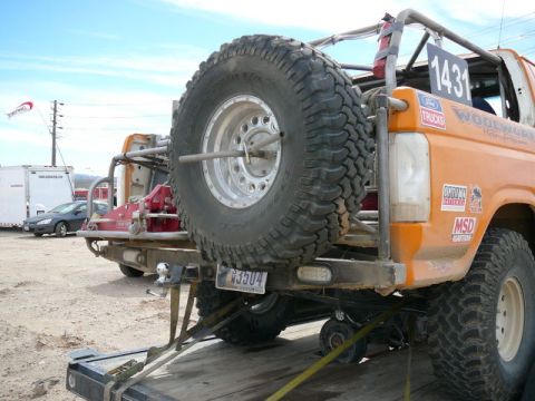 1988 Ford Bronco - An orange off-road SUV is seen from the rear, secured to a trailer with straps.