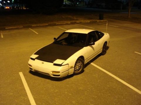 1991 Nissan 240SX - A white 1991 Nissan 240SX coupe is parked in a lot at night, showing its black hood.