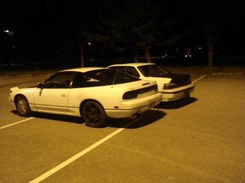 1991 Nissan 240SX - A white 1991 Nissan 240SX coupe is parked next to a dark sedan in a parking lot at night.