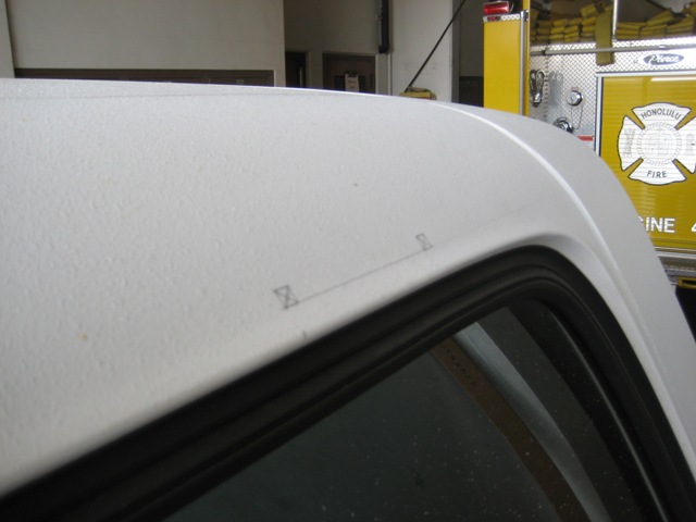 White vehicle roof corner with pencil marks, yellow Honolulu fire truck in background garage
