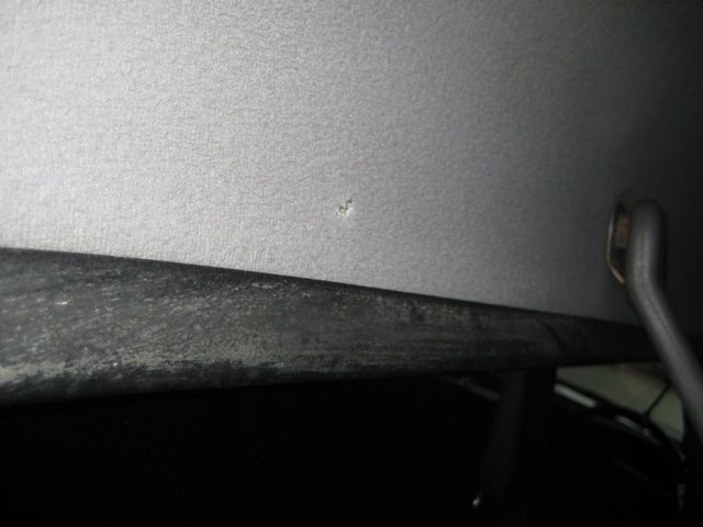 Gray headliner close-up with small tear near dark trim edge inside a vehicle