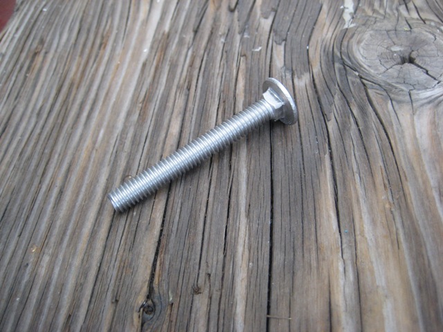 Silver carriage bolt with domed head and threaded shank on weathered gray wood plank