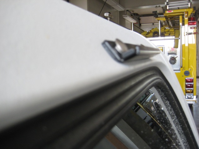 Close-up of a white vehicle's roof trim with a yellow fire truck in the background