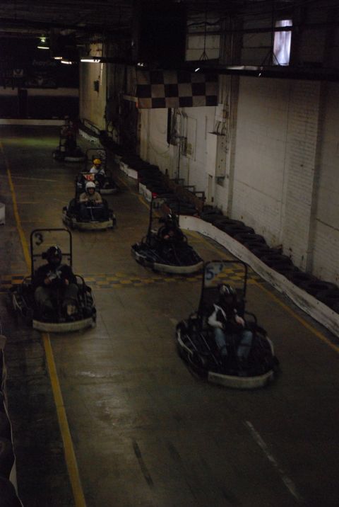 1993 Ford Probe - Several go-karts are racing on an indoor track under dim lighting, with a checkered flag visible.