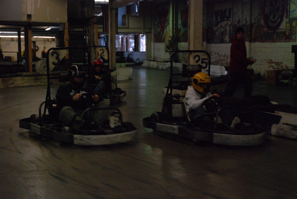 Go-karts with drivers on an indoor track, numbers 3 and 25 visible on karts
