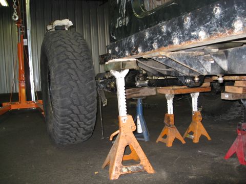 1994 Jeep YJ - Jeep YJ frame undergoing maintenance, supported by multiple jack stands and a large tire.