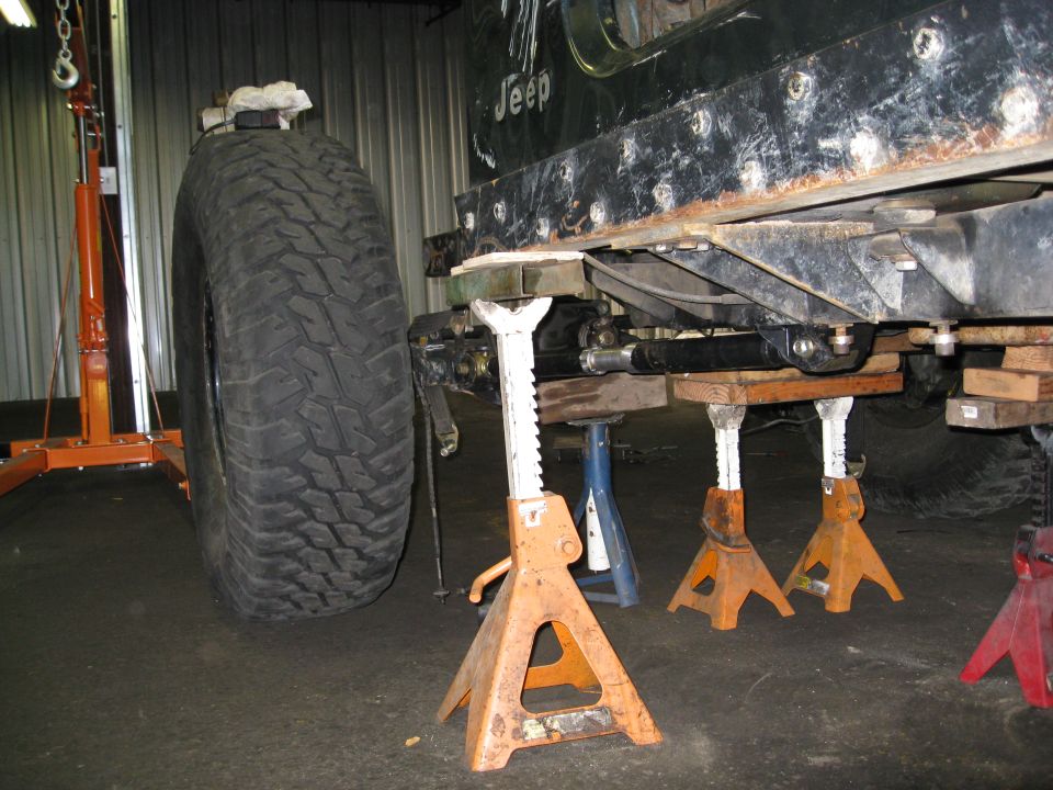 1994 Jeep YJ frame supported by jack stands, large off-road tire visible. 'Jeep' text on frame