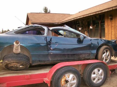 1996 Ford Probe - This heavily damaged coupe is being transported on a trailer, with significant damage to its windows and body panels.
