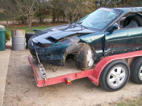 1996 Ford Probe - A damaged green 1996 Ford Probe is loaded onto a trailer, ready for transport.