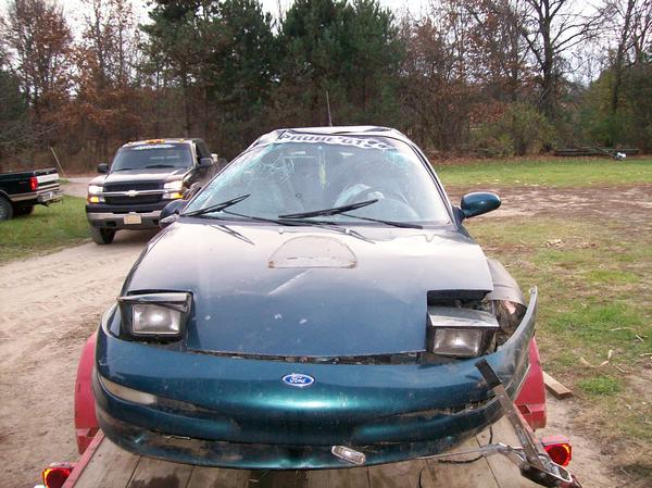 1996 Ford Probe with damaged front end on a trailer, another truck visible behind it