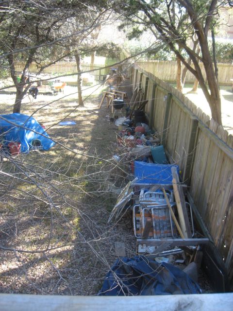1986 Ford Bronco - A cluttered backyard scene with a wooden fence and various items stored along it.
