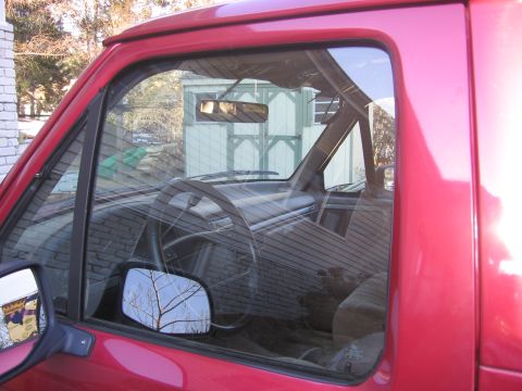 1995 Ford Bronco - View into the cab of a red pickup truck, with a shed reflected in the windshield.
