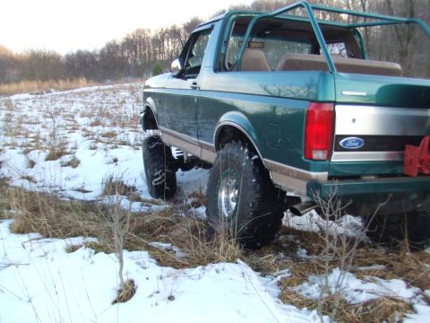 1996 Ford Bronco - Rear view of a lifted green Ford Bronco with off-road tires in a snowy, grassy field.