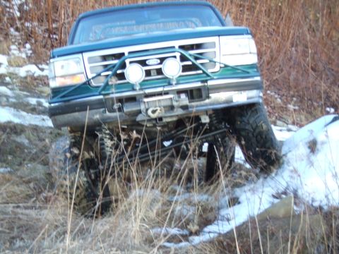 1996 Ford Bronco - Modified 1996 Ford Bronco navigates a snowy, grassy incline with large off-road tires.