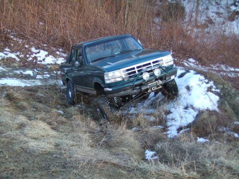 1996 Ford Bronco - This modified Ford Bronco is navigating a challenging off-road terrain with snow and rocks.