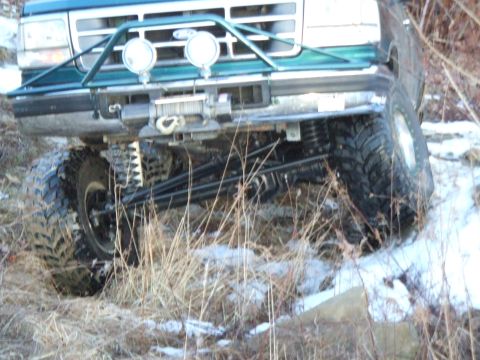 1996 Ford Bronco - Low front-corner view of a lifted teal green Ford truck articulating over snowy brush, with one front tire stuffed up into the fender and t…