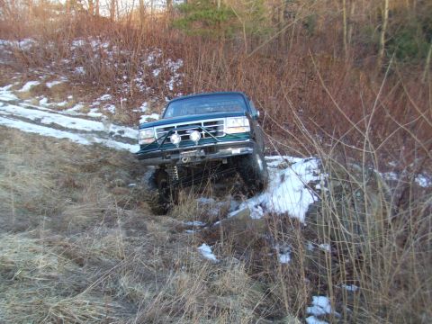 1996 Ford Bronco - A dark green 1996 Ford Bronco navigates a challenging off-road course with snow and dry grass.