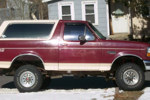 1993 Ford Bronco - A maroon and tan 1993 Ford Bronco is parked on a snowy street, viewed from the side.