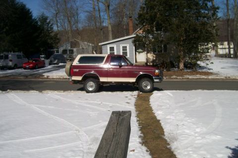 1993 Ford Bronco - A maroon and tan 1993 Ford Bronco is parked on a street covered in snow.