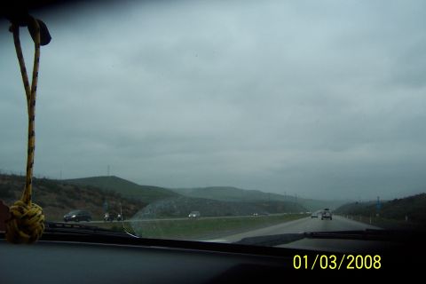 1990 Ford Bronco - A highway stretches through rolling hills under a cloudy sky, with several vehicles visible on the road.