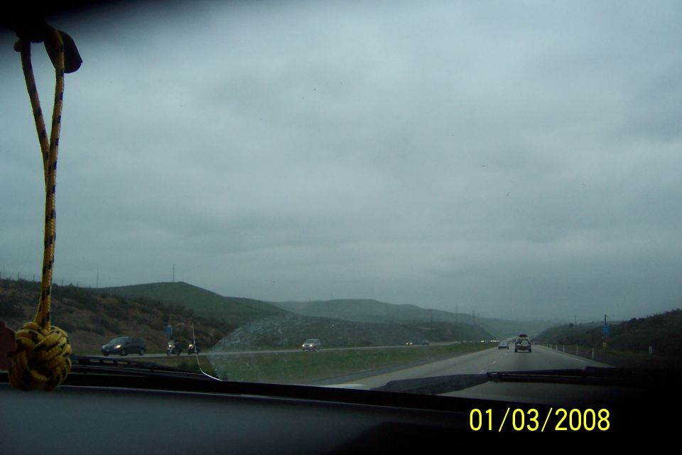View from inside a vehicle looking out at a highway on a cloudy day, with a rope hanging from the rearview mirror