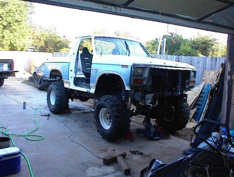 1981 Ford Bronco - A modified pickup truck is undergoing repairs, missing its front bumper and grille.