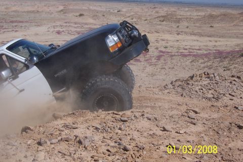 1990 Ford Bronco - A black 1990 Ford Bronco tackles a challenging off-road course, kicking up dust as it maneuvers.