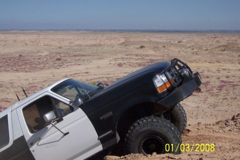 1990 Ford Bronco - This Ford Bronco is navigating a sandy, desert-like terrain with a clear sky in the background.