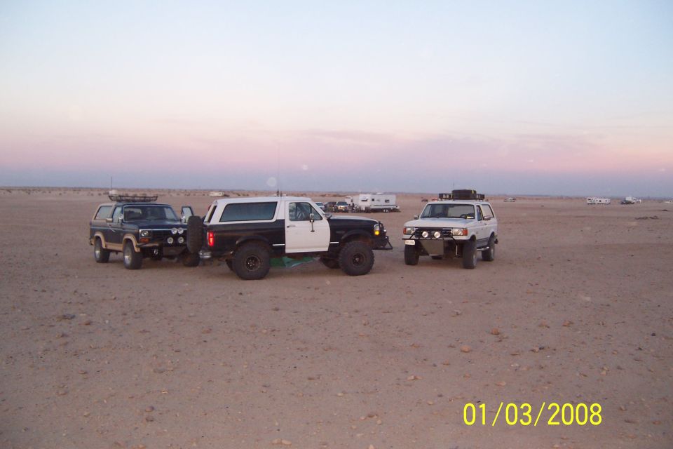 Two-tone Ford Bronco with roof rack and off-road lights, parked in desert