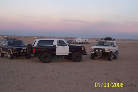 1990 Ford Bronco - Three Ford Broncos are parked in a desert setting during twilight, with RVs visible in the background.