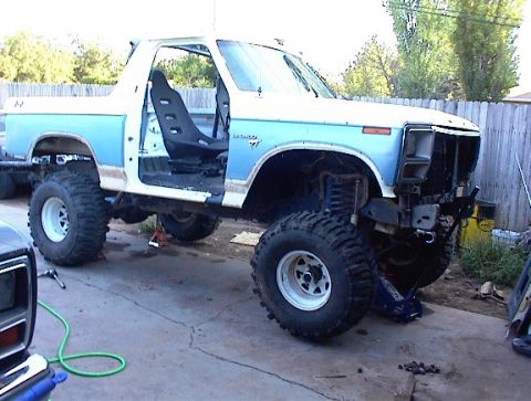 1981 Ford Bronco - This lifted 1981 Ford Bronco is undergoing modifications, with its front end partially disassembled and large off-road tires installed.