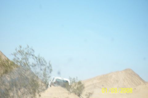 1990 Ford Bronco - A white SUV navigates a sandy terrain, with desert landscape and clear skies visible.