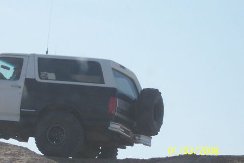 1990 Ford Bronco - This Ford Bronco is shown from the rear, with a spare tire on the back, driving on an incline.