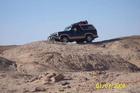 1990 Ford Bronco - A Ford Bronco navigates a sandy incline under a clear blue sky.