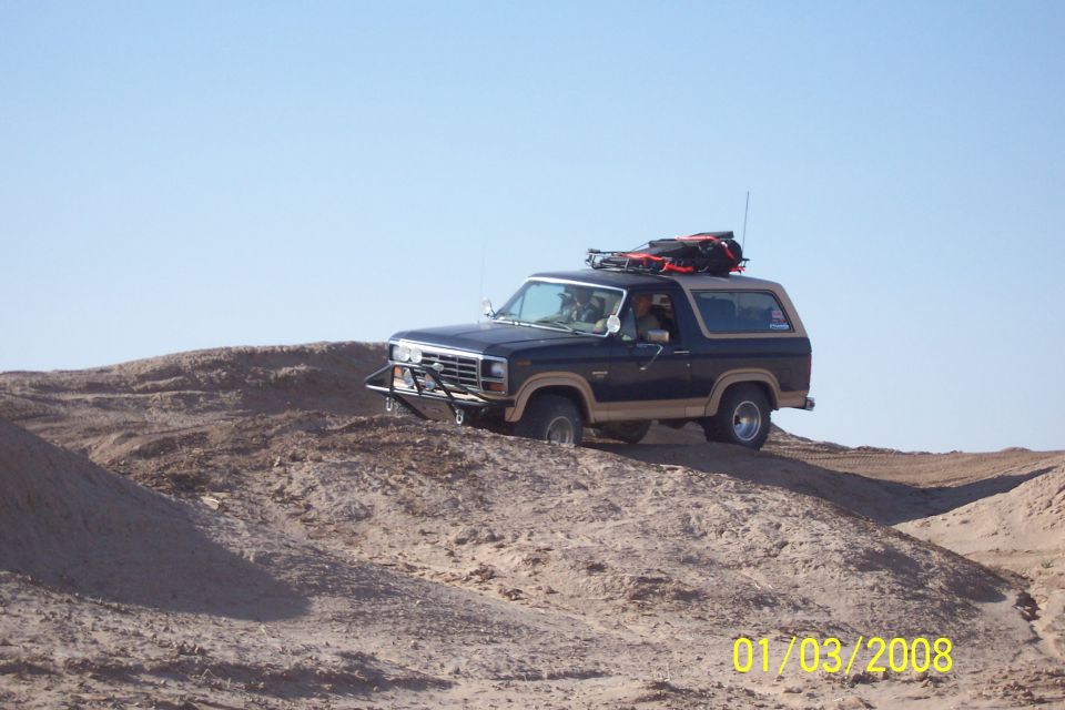 Dark blue and tan Ford Bronco with roof rack driving on a dirt hill