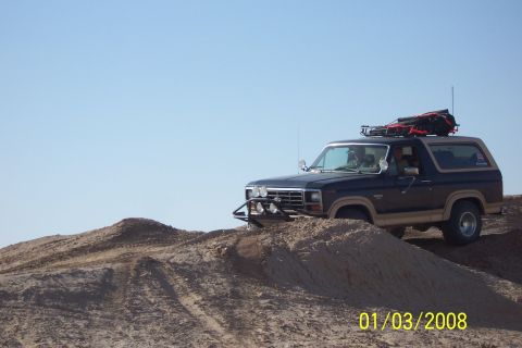 1990 Ford Bronco - Ford Bronco navigates sandy terrain under a clear blue sky.