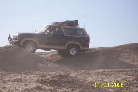 1990 Ford Bronco - This Ford Bronco is navigating a desert landscape, with its tires gripping the sandy terrain.