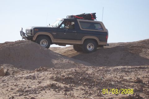 1990 Ford Bronco - This Ford Bronco is navigating a sandy, off-road terrain under a clear sky.