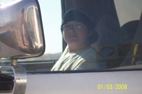 1990 Ford Bronco - A person looks out from inside a vehicle, with the side mirror reflecting the scene.