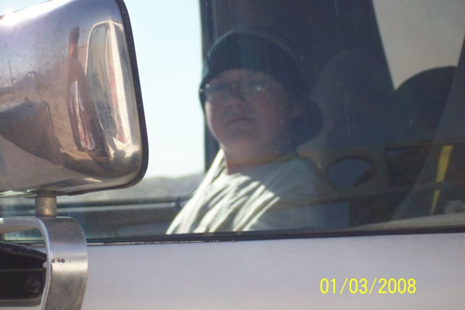 person wearing glasses and a hat looks out the window of a vehicle, side mirror in foreground