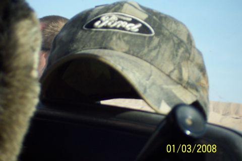 1990 Ford Bronco - A camouflage baseball cap with a Ford logo is visible in the foreground, with a person's head and a portion of a vehicle's interior.
